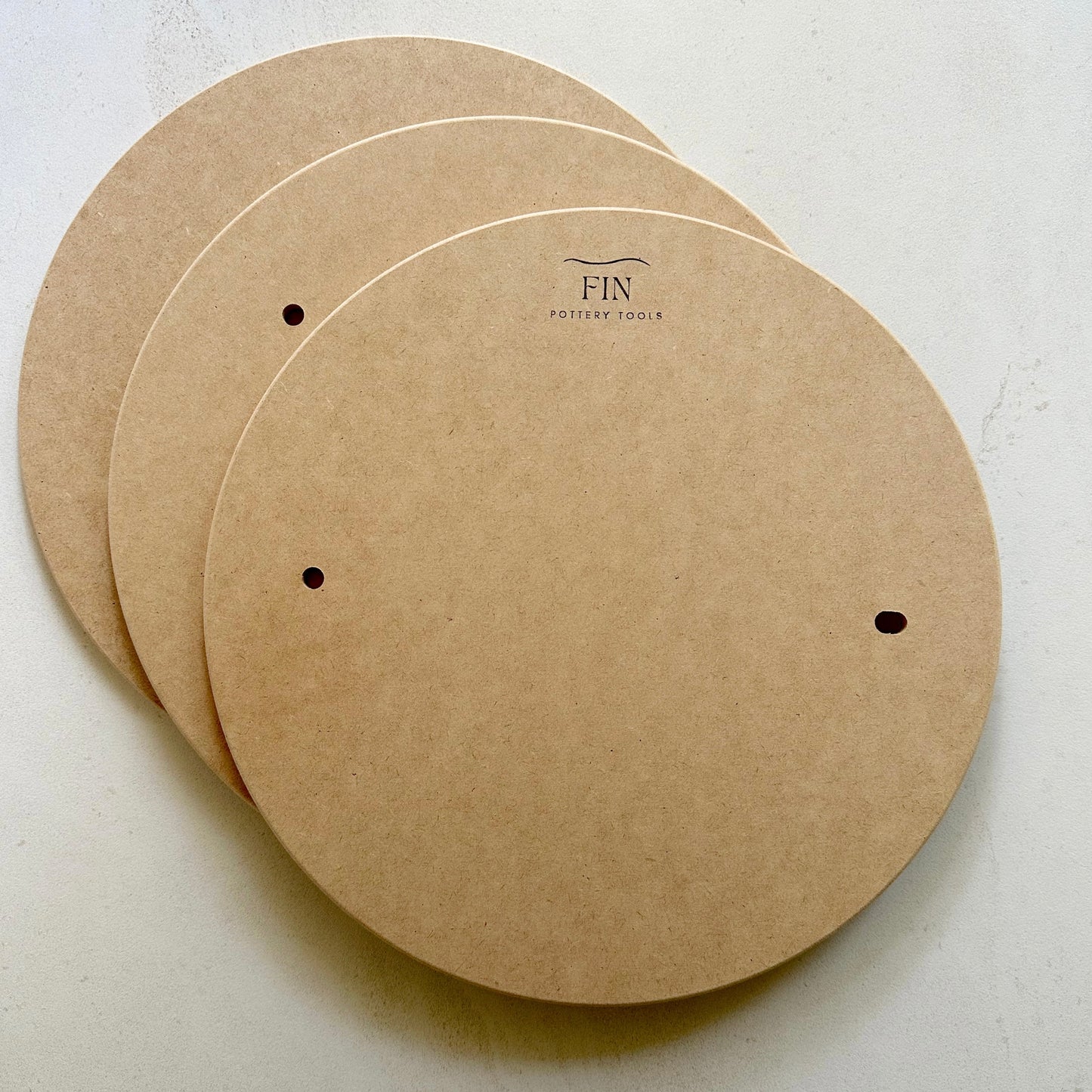 Three MDF pottery bats with pin holes. compatible with Venco or Shimpo wheels, placed on a flat surface.