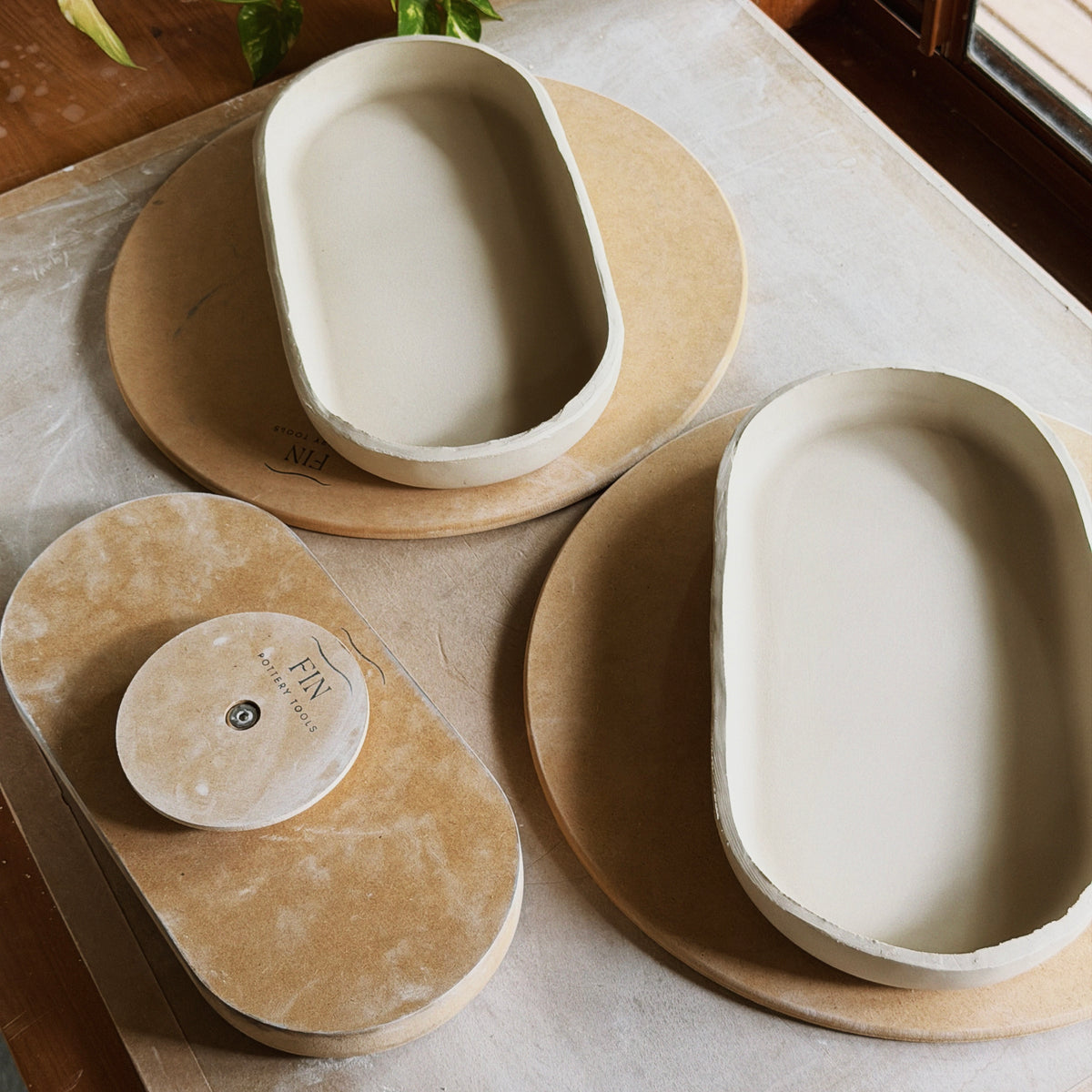 Three handmade oblong ceramic dishes made using the Fin Pottery Tools Oblong Large Pottery Forms, in white clay, displayed on two bats. 